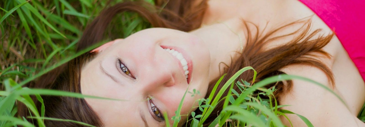 Smiling woman lying in grass, showcasing bright teeth and a relaxed expression, symbolizing spring renewal and cosmetic dentistry at Fishinger Dental.