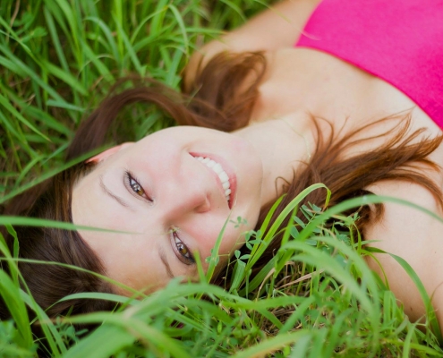 Smiling woman lying in grass, showcasing a bright and refreshed smile, relevant to cosmetic dentistry and enhancing aesthetic appearance at Fishinger Dental.